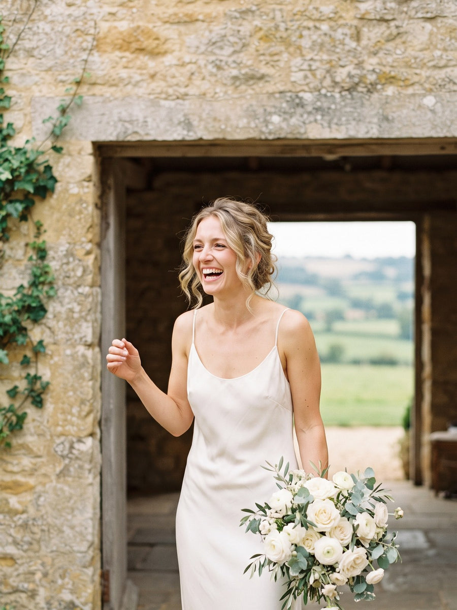 A bride laughing in the doorway of a Cotswolds stone barn